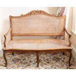 A Louis XV style two seat settee, 20th century, with caned back and seat, on three scroll carved