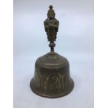 A 20th century Indian brass bell, the side engraved panels of figures, with handle fashioned with