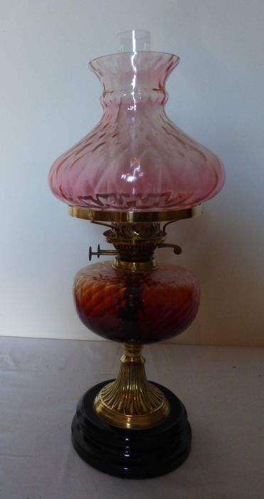 A tall Victorian oil lamp. Brass based with Cranberry and Amber glass. sat on a black glass