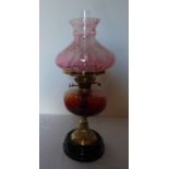 A tall Victorian oil lamp. Brass based with Cranberry and Amber glass. sat on a black glass