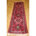 A mid 20th century Iranian wool runner, woven with twin latch hook lozenge medallions on a madder