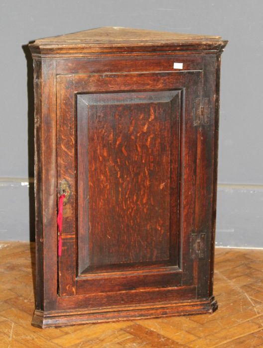 A George III oak wall mounting corner cupboard of small size, the fielded panel door enclosing three