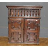 An 18th century and later oak wall cupboard, the plank top over a hinged spindle guarded shelf and a