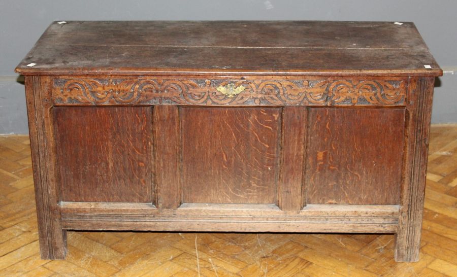 An 18th century oak coffer, the plank top with later hinges, over a scroll carved frieze and three