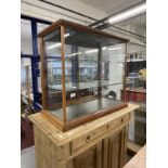 Early 20th cent. Display case, sliding glass doors to the back, two glass shelves on a moulded base.