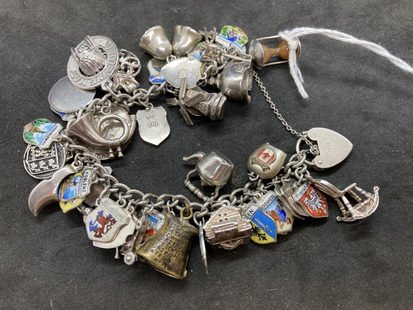 Hallmarked Silver: Bracelet with forty plus charms attached, having a padlock fastening and chain.