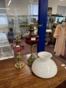 Victorian oil lamps brass bases, red glass reservoirs, one with white shade. 23½ins. and 20ins. (2)