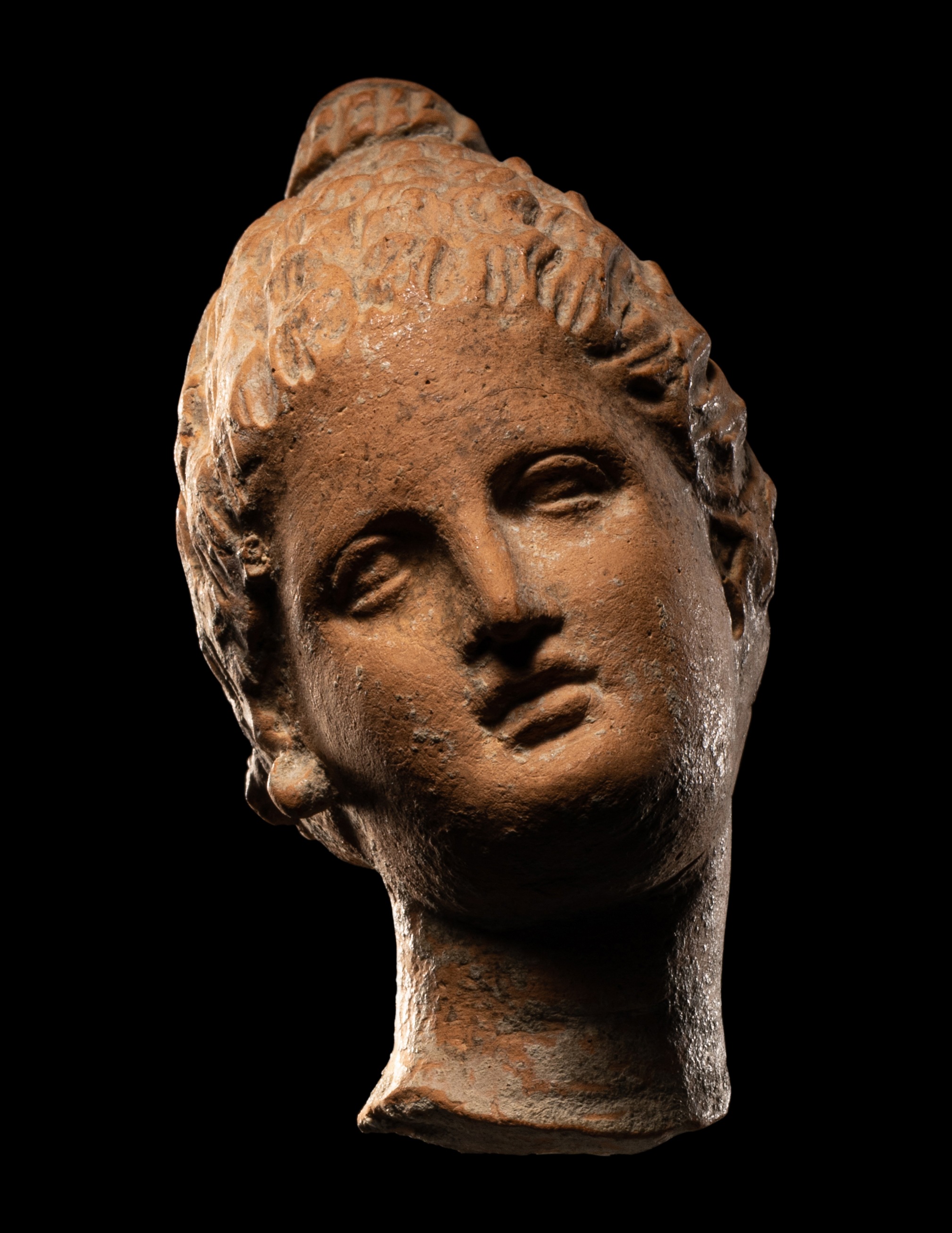 A Greek Terracotta Female Head with Melon Coiffure Height 3 inches (7.6 cm).