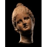 A Greek Terracotta Female Head with Melon Coiffure Height 3 inches (7.6 cm).
