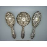 A silver backed hand mirror and three brushes