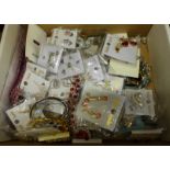 A box of packaged costume jewellery including bangles, brooches and earrings