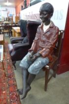 A life size Goldscheider style hand painted fibreglass figure of a seated young boy