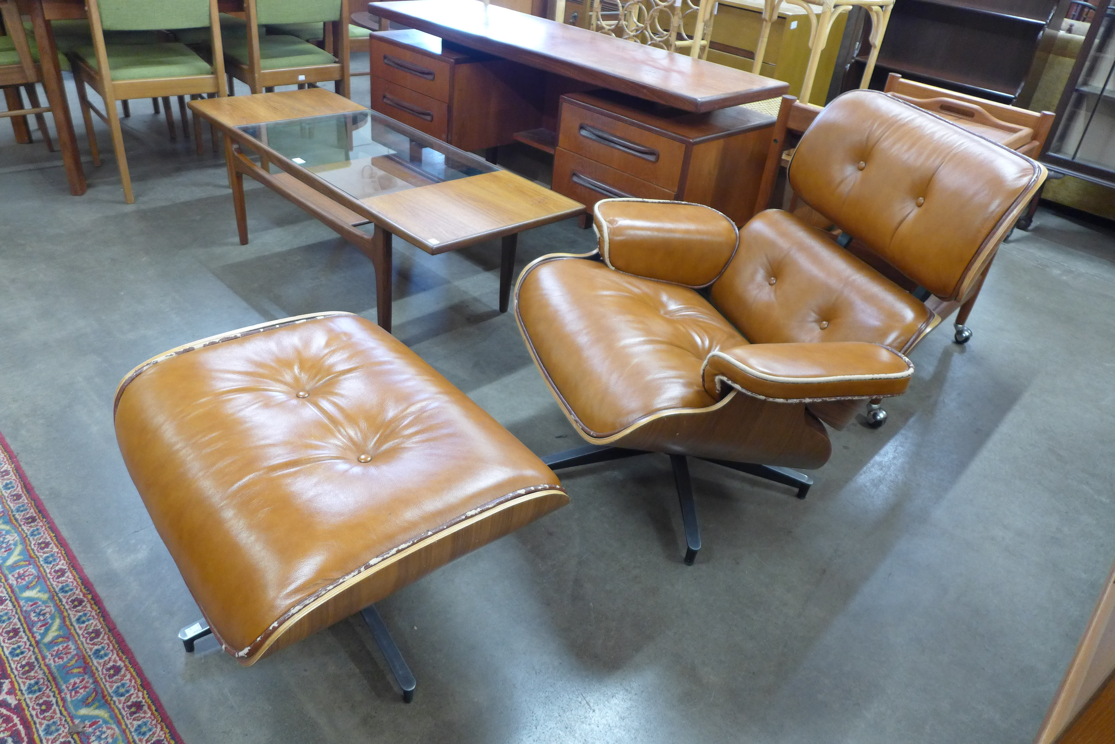 A Charles & Ray Eames style tan leather armchair and stool