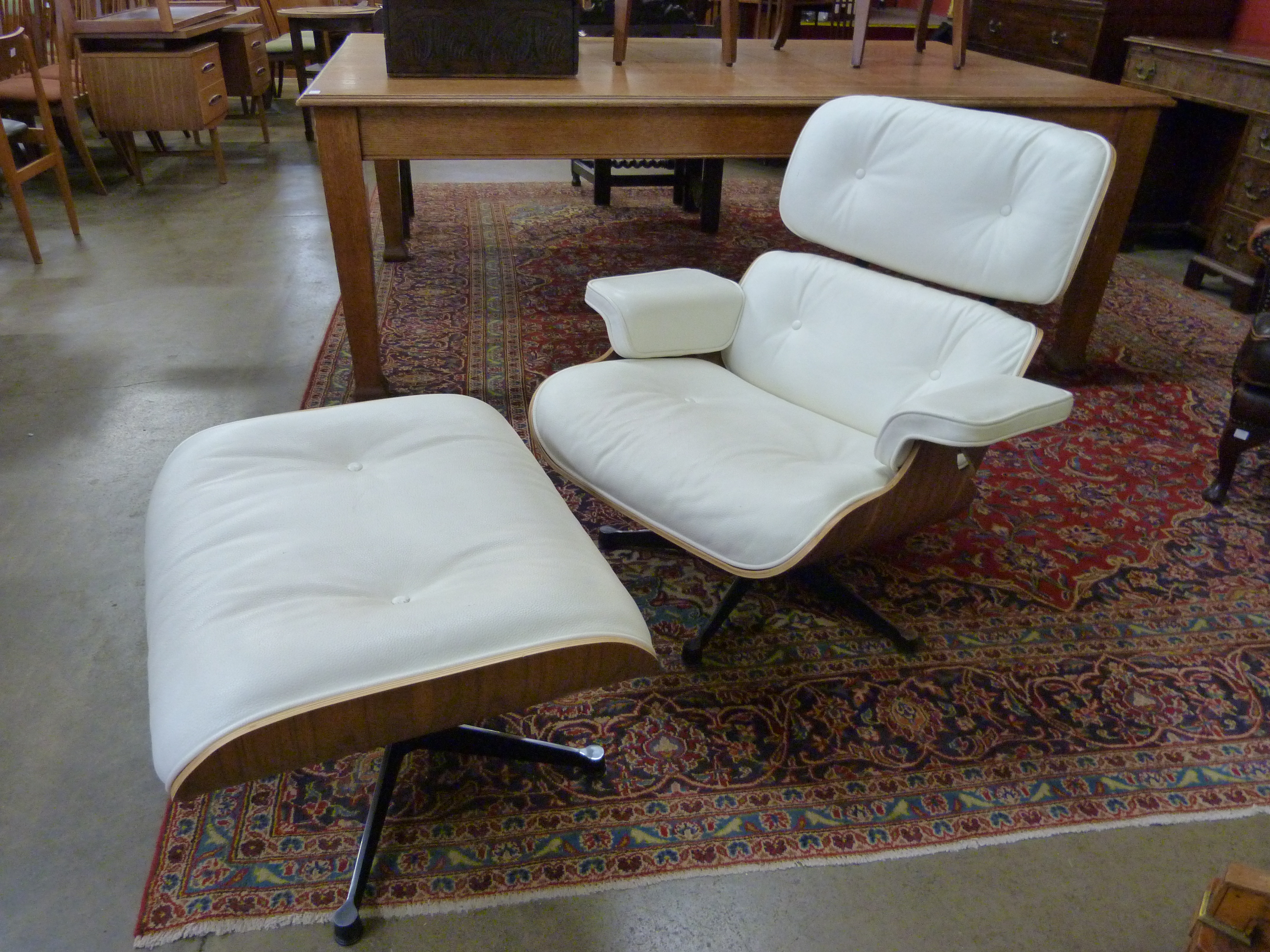 A Charles & Ray Eames style simulated rosewood and cream leather revolving lounge chair and stool
