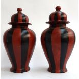 A pair of terracotta lidded urns, painted in red and black stripes, each 44cmH