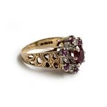 A 9ct gold ring set with a central garnet surrounded by smaller garnets and illusion set diamond