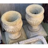 A pair of composite stone urns half gadrooned, each on square plinth base