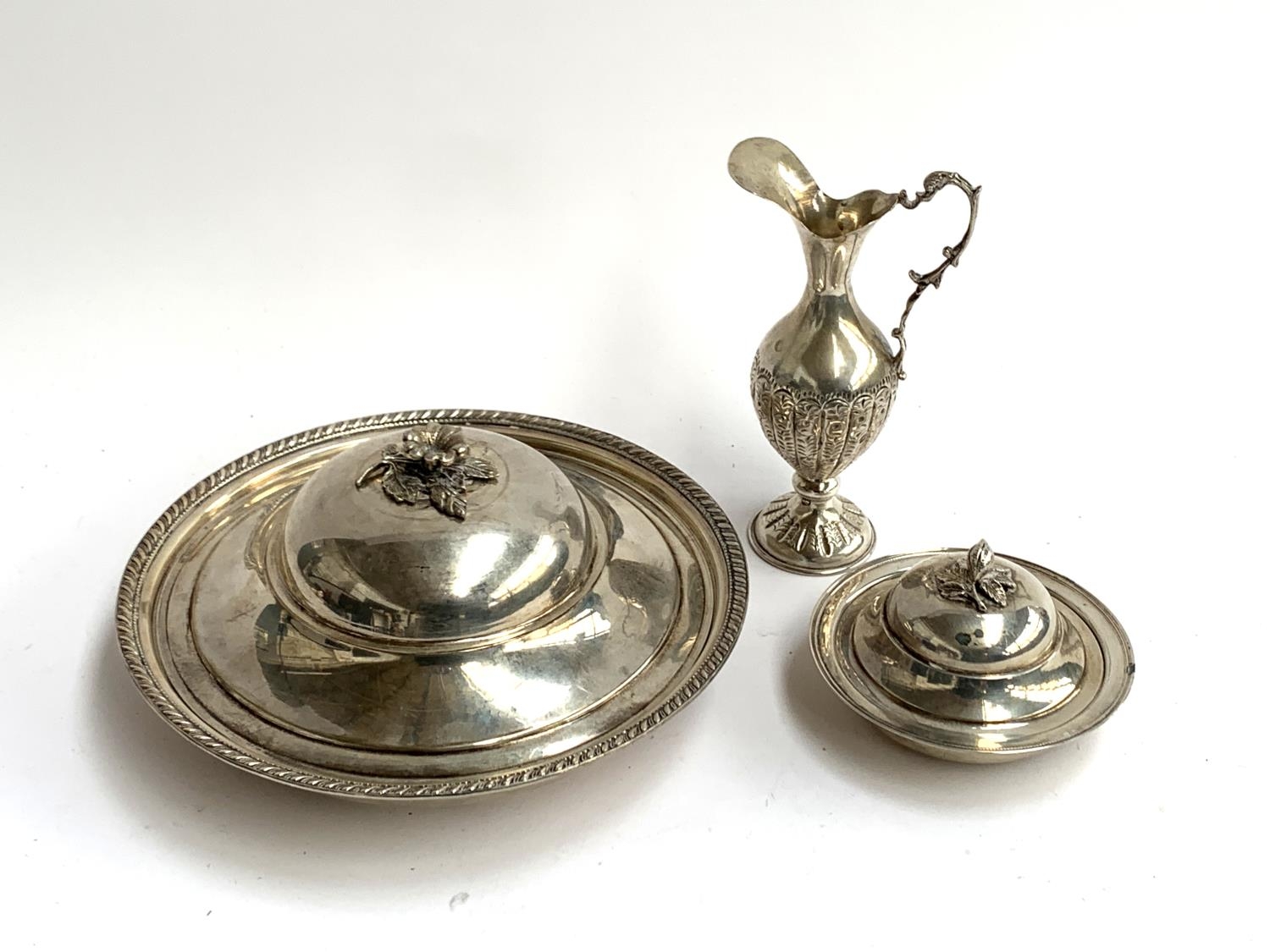 Three white metal items, to include two circular lidded dishes, each with foliate finial, both