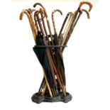A cast iron stick stand containing a quantity of various walking sticks and vintage umbrellas