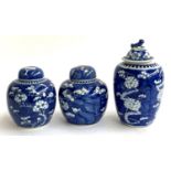 A lot of three Chinese ginger jars with blue and white prunus design, the tallest with foo dog cover