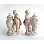 A pair of Schierholz porcelain figures of putti holding an encrusted posy of flowers beside a lidded