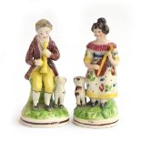 A pair of Staffordshire figures of a man with a horn and a lady with a mandolin, each sitting on a