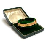 An Edwardian 9ct gold bangle of buckle form, foliate engraved decoration, with safety chain,