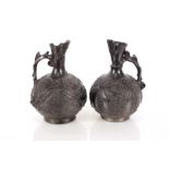 A pair of black glazed pottery ewers, having profuse leaf decoration and scrolled handles, 28cm high