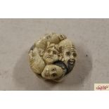 A carved bone Netsuke decorated with faces