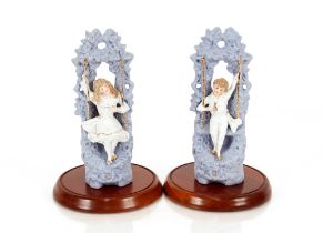 A pair of blue bisque ware hollow figures, of a boy and girl on swings under later glass domes