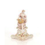 A Dresden style porcelain figure, of a maiden with basket of flowers seated on a plinth, 29cm high