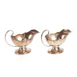 A pair of silver sauce or gravy boats, of panelled form with loop handles raised on oval oak