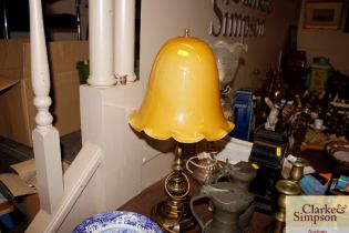 A brass table lamp with yellow glass opaque shade