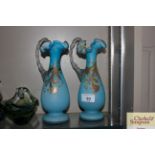 A pair of blue glass and enamel decorated ewers