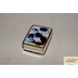 A small white metal pill box and enamel decorated