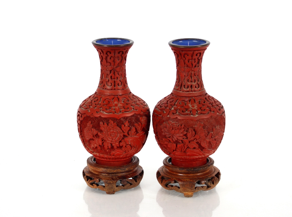 A pair of Chinese cinnabar lacquered vases, on wooden stands of baluster form with blue enamel