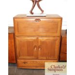 A light Ercol secretaire cabinet, drop flap compar