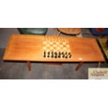 A teak coffee table with chequerboard inset top, fitted with drawer and contents of chessmen, raised