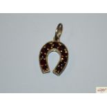 A small yellow metal horse shoe pendant set garnet