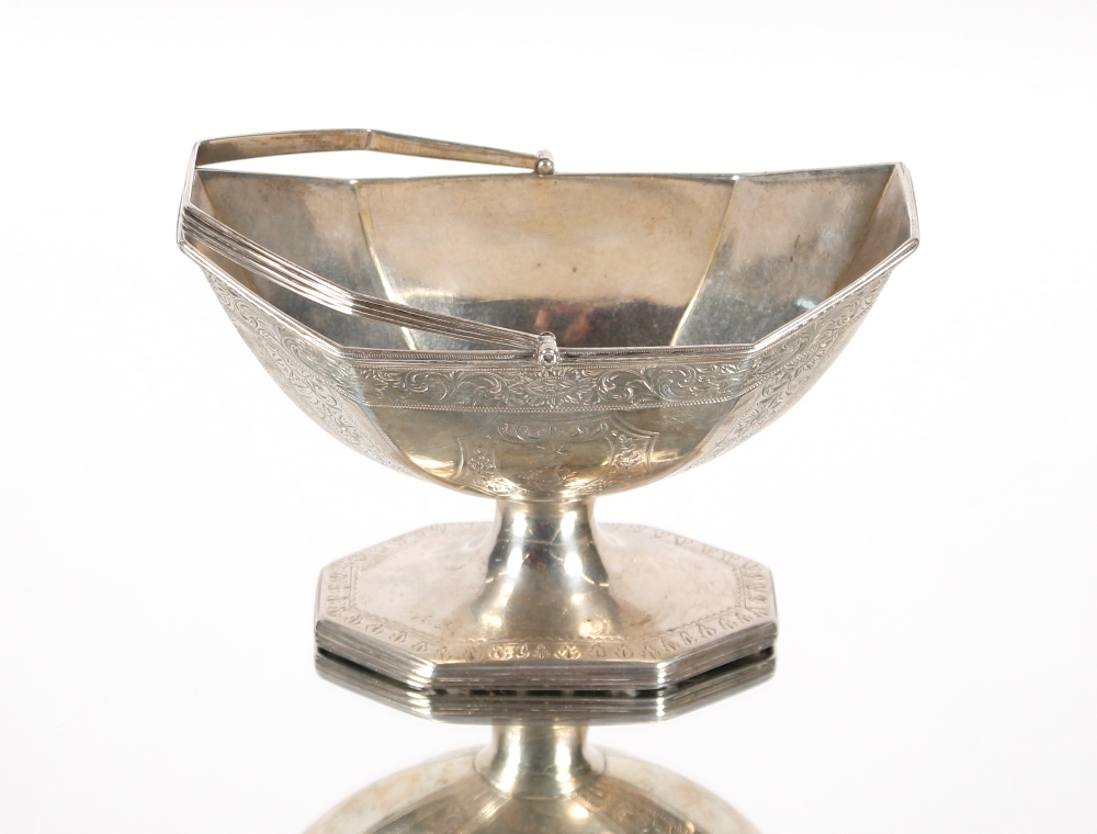 A George III silver swing handled basket with foliate scroll decoration and central family crest rai