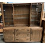 An Ercol medium elm wall unit with two upper glazed door cabinets flanking three glass shelves over