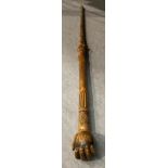 A wood walking stick - the handle depicting a hand holding a cricket ball,