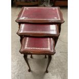 A mahogany nest of three coffee tables with red tooled leather top and protective glass inserts