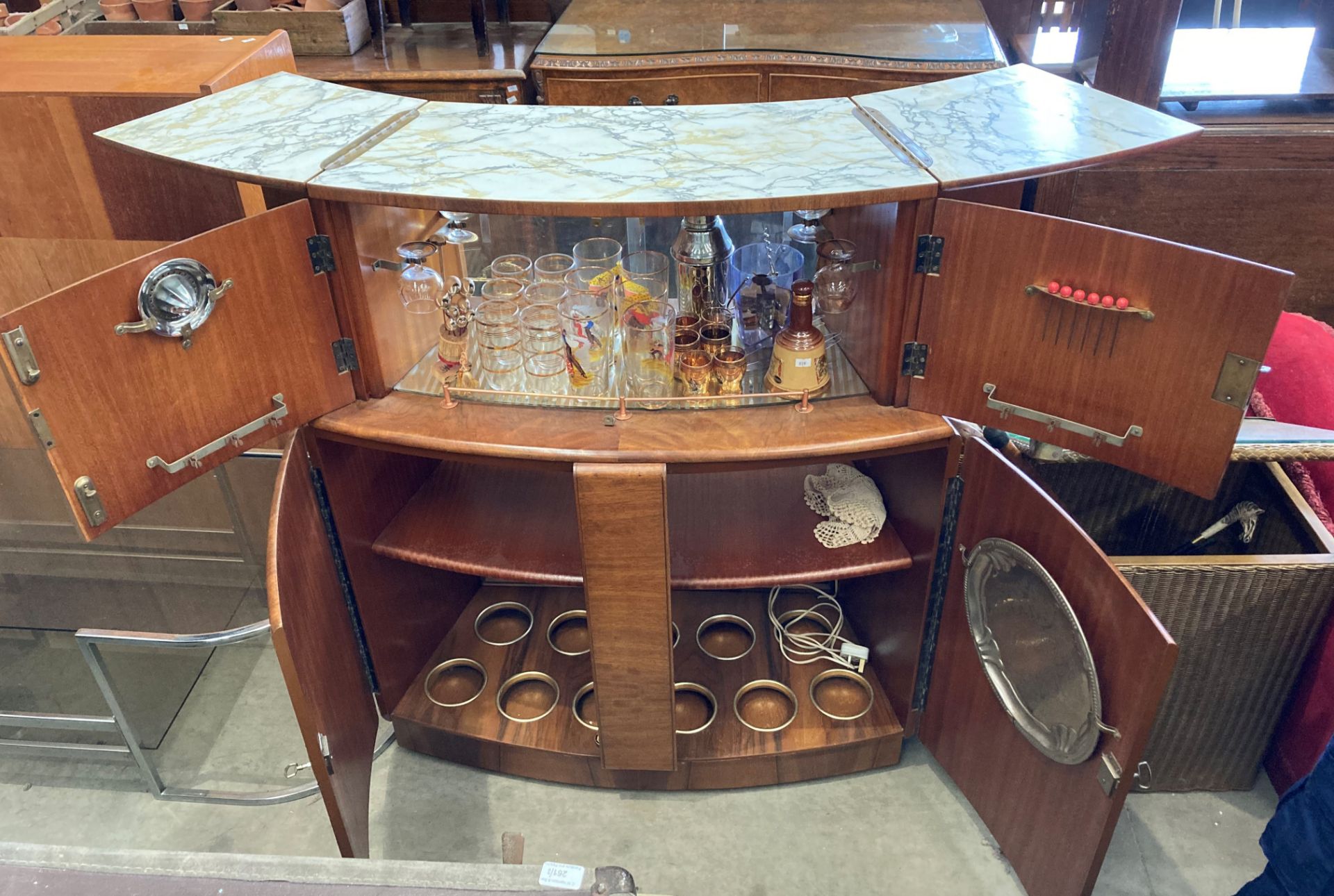 A 1950s walnut finish curved double sided bar with marble effect folding top over two doors and