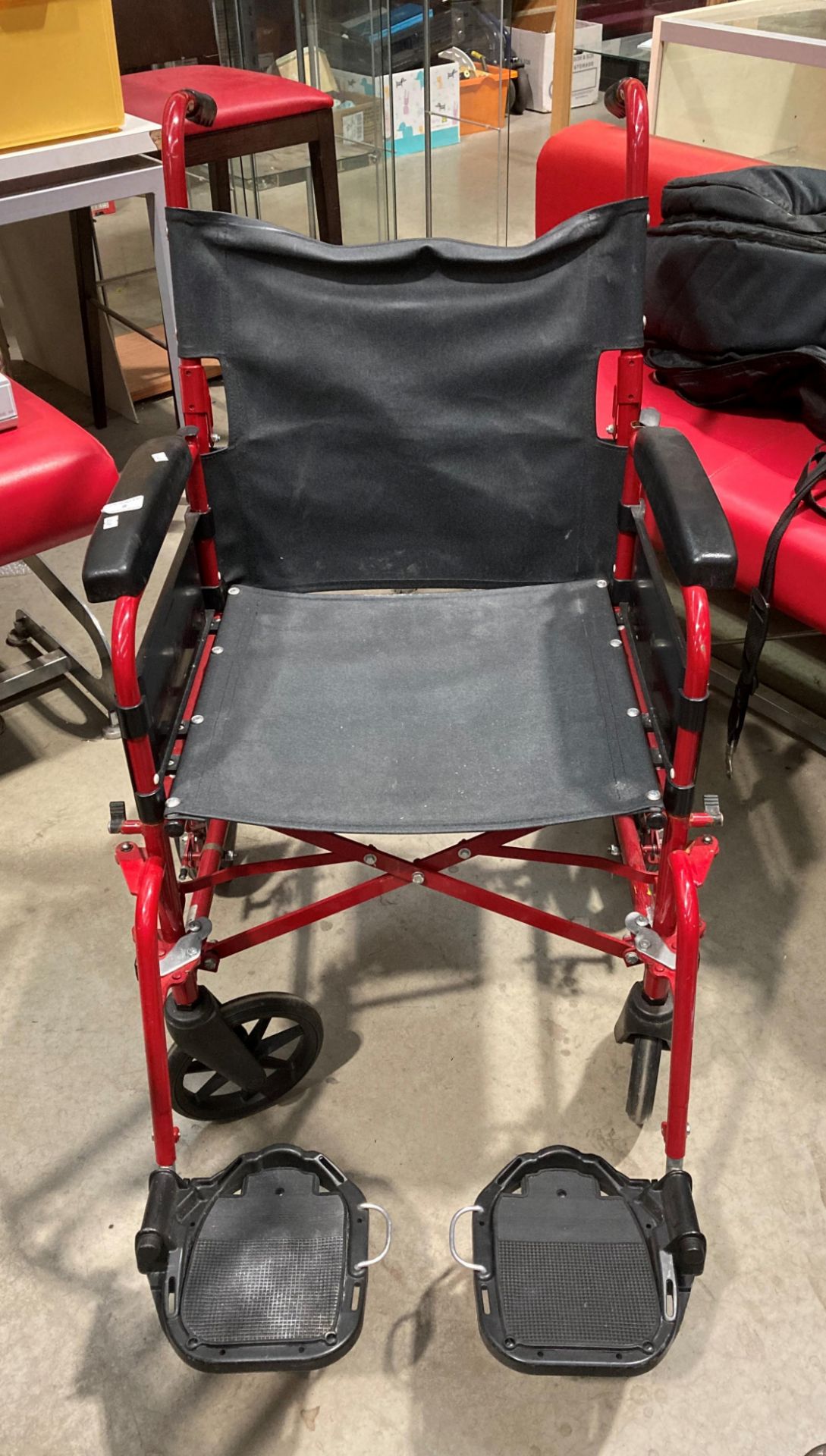 A Remploy red metal framed four wheel wheelchair with foot rests.