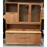 A teak wall unit on castors with two glazed upper doors and fall front cabinet over two drawer two