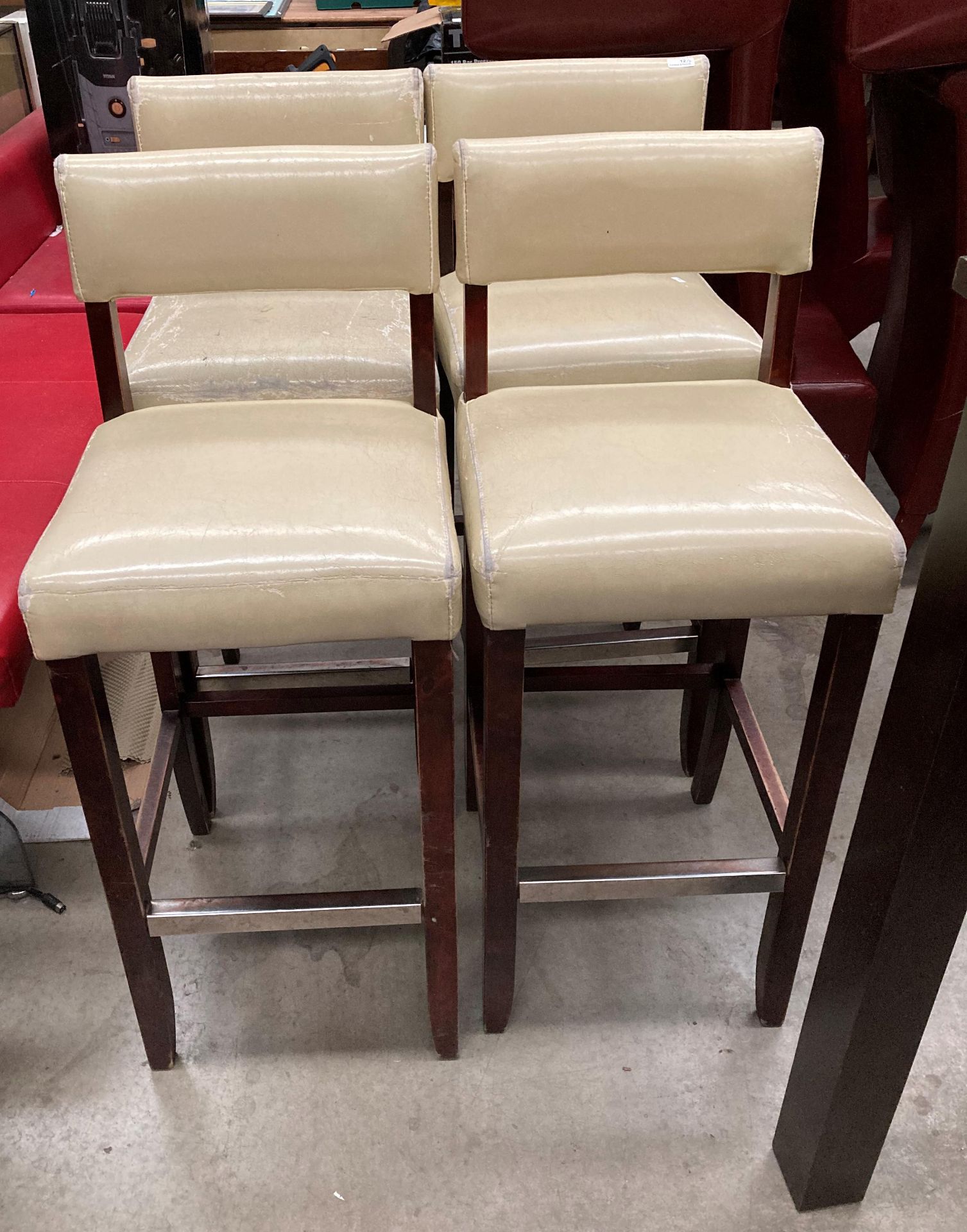 A set of four beige leather effect high bar stools - the upholstery is worn in places on all the