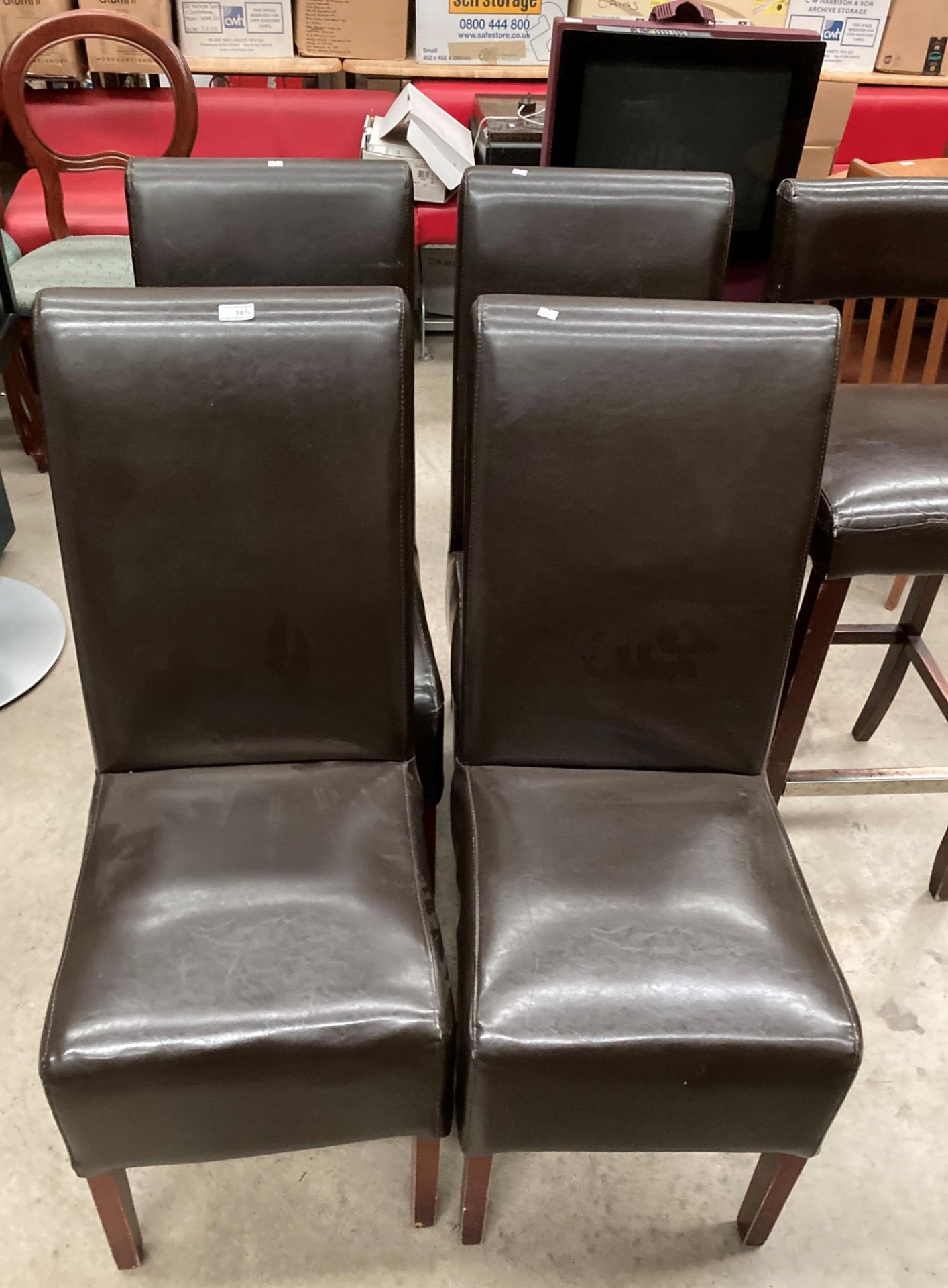 A set of four dark brown leather effect upholstered dining chairs.