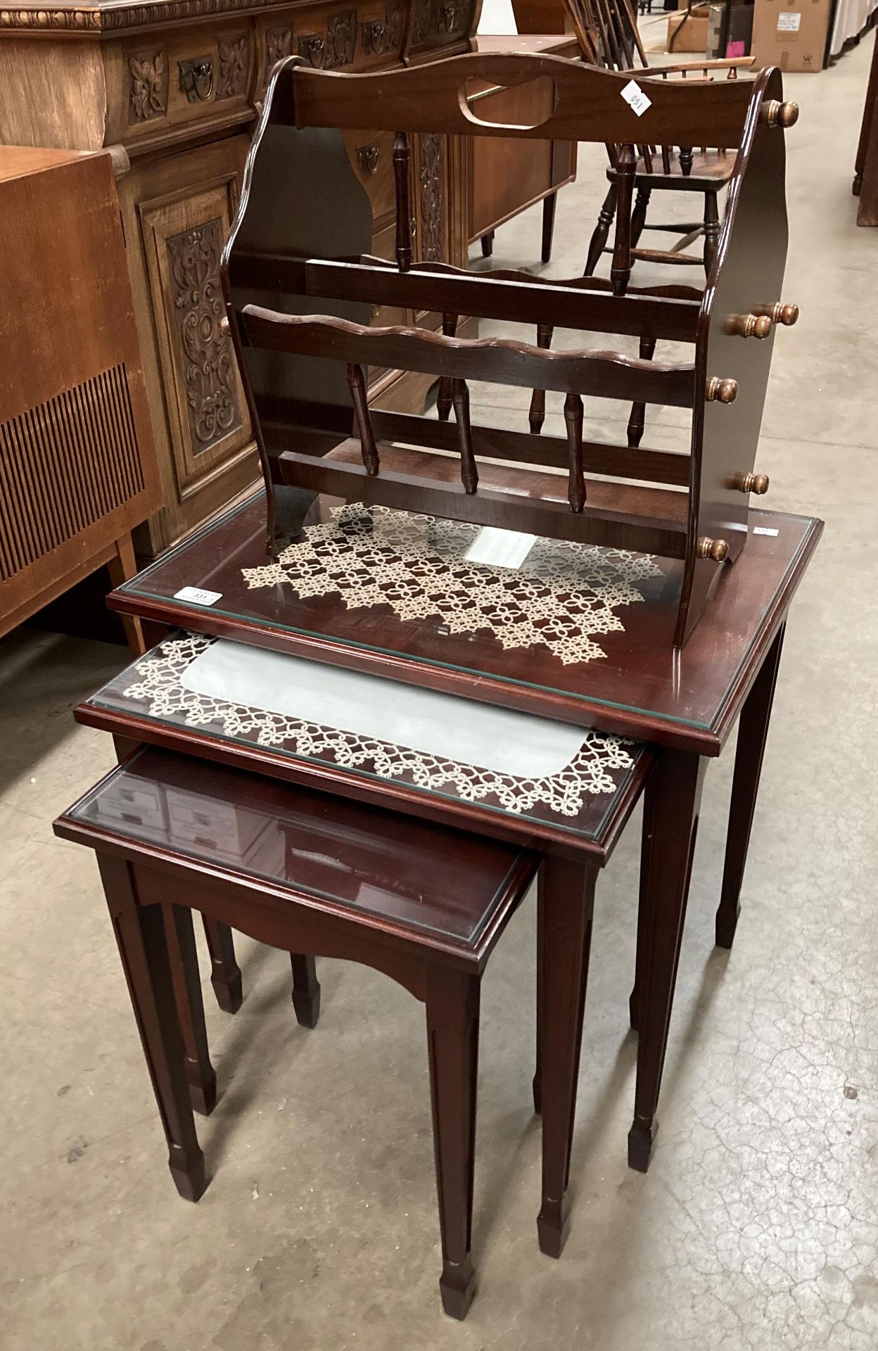 A nest of three mahogany tables with glass protective tops and a mahogany magazine rack