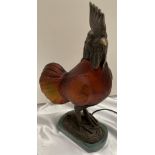 A metal and brown glass table lamp in the form of a cockerel on marble base,